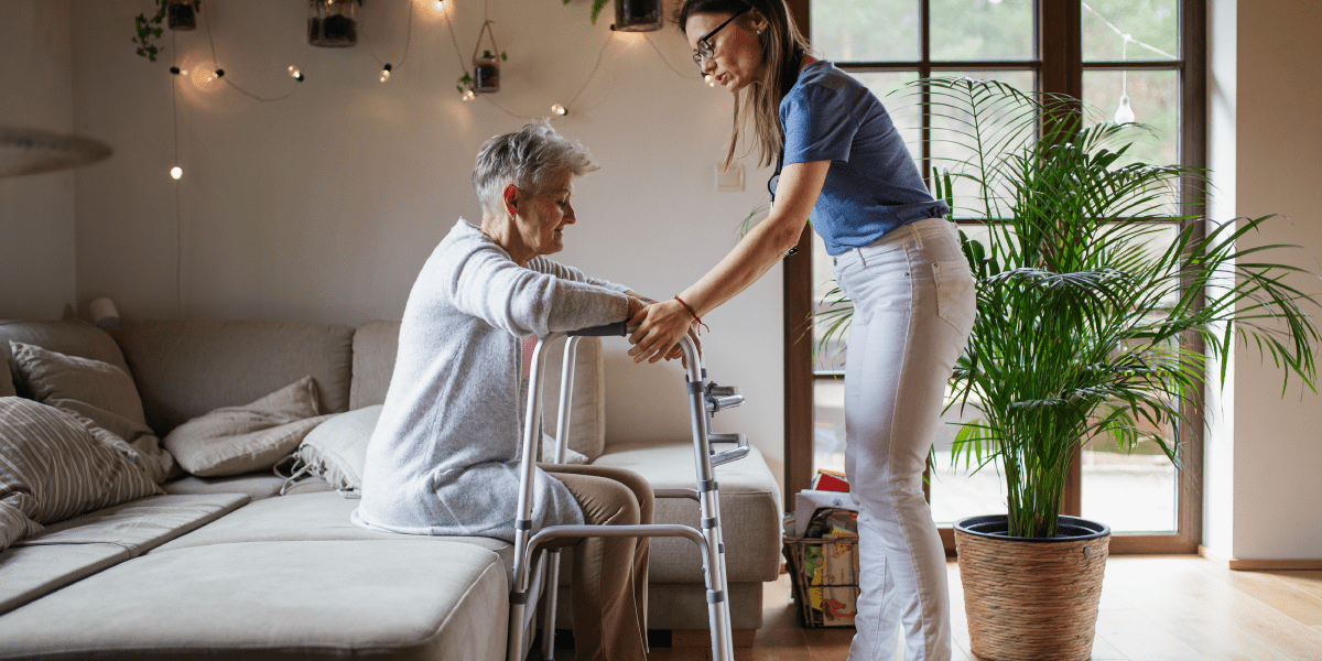 caregiver helping senior woman stand with walker