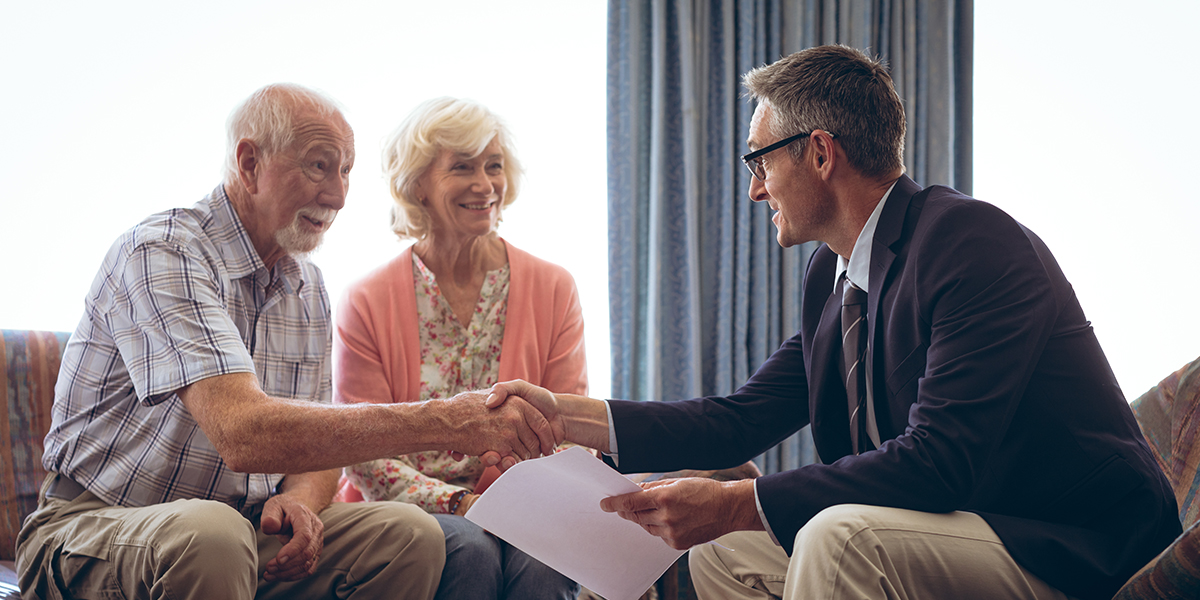 Front view of matured Caucasian male lawyer interacting with senior Caucasian couple at retirement home Both men shaking hands